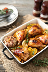 Baked chicken legs and potatoes with oranges, garlic and onions in a baking dish on a light gray wooden culinary background closeup	