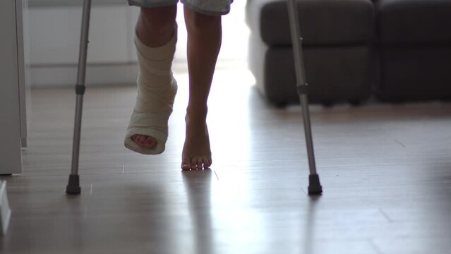 Young woman with broken leg in plaster cast trying to walk with crutches in living-room. Physical injury, bone fracture and accident,