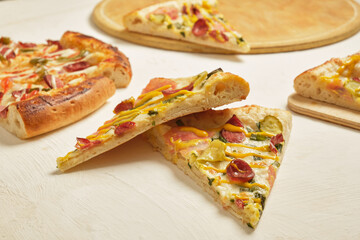 several slices of pizza with sausage and jalapeno peppers on a light background