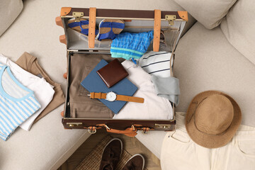 Open suitcase with different men clothes and accessories on sofa, top view