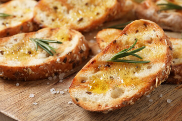 Tasty bruschettas with oil and rosemary on wooden board, closeup