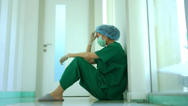 Side view of stressed and overworked female doctor medical worker surgeon sitting on the floor near the operating room in hospital and take off the mask
