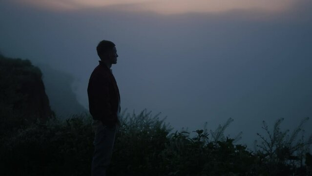 Relaxed guy looking mountain horizon in morning fog. Man standing on cliff