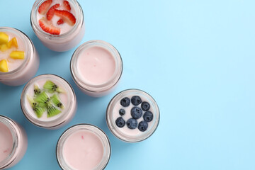 Obraz na płótnie Canvas Tasty yogurt in glass jars and ingredients on light blue background, flat lay. Space for text
