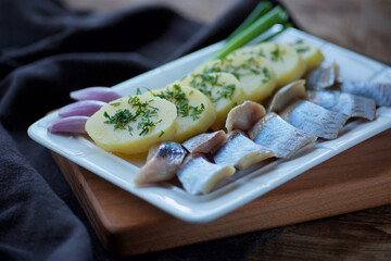 Fish herring, sliced into pieces and potatoes lie on a white plate with greens.