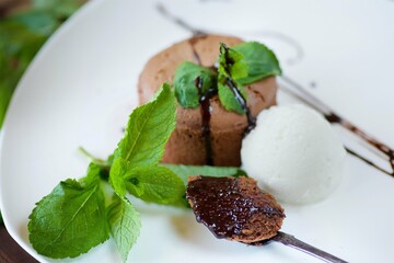 A cupcake or pancake with chocolate filling lies on a plate of ice cream. The dish is decorated for serving