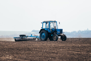 Obraz premium The tractor processes the field in spring. combine harvester in work on sowing wheat