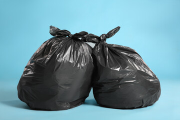 Black trash bags full of garbage on light blue background