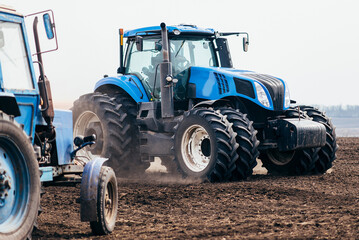 Obraz premium The tractor processes the field in spring. combine harvester in work on sowing wheat