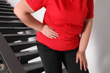 Overweight mature woman suffering from pain in right side on stairs indoors, closeup