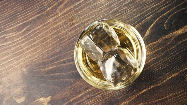 Glass with whiskey and ice cubes rotates. Closeup slow motion fullhd footage