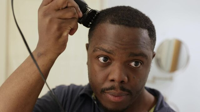 Personal hygiene, African American or black man at home in bathroom using clipper or trimmer to cut his own hair as a barber would