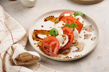 Traditional italian salad caprese consisting of slices red tomatoes, fresh basil and mozzarella cheese with balsamic vinegar dressing on concrete background, wooden pepper and salt mills