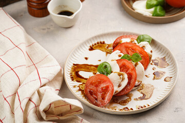 Traditional italian salad caprese consisting of slices red tomatoes, fresh basil and mozzarella cheese with balsamic vinegar dressing on concrete background, wooden pepper and salt mills