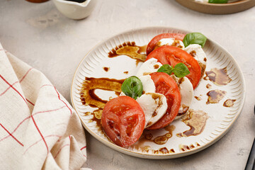 Traditional italian salad caprese consisting of slices red tomatoes, fresh basil and mozzarella cheese with balsamic vinegar dressing on concrete background, wooden pepper and salt mills