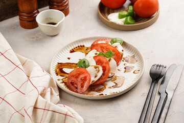 Traditional italian salad caprese consisting of slices red tomatoes, fresh basil and mozzarella cheese with balsamic vinegar dressing on concrete background, wooden pepper and salt mills