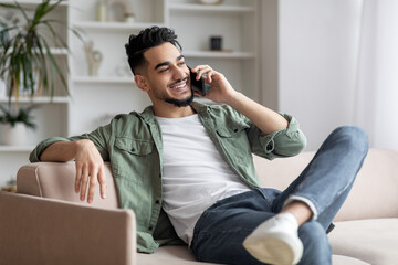 Cheerful arab guy having phone call while relaxing on couch at home