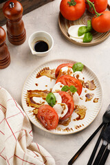 Fototapeta na wymiar Traditional italian salad caprese consisting of slices red tomatoes, fresh basil and mozzarella cheese with balsamic vinegar dressing on concrete background, wooden pepper and salt mills