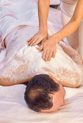 Obraz na płótnie Canvas A woman healer performs a ritual with salt, rubs the back of a lying man with salt. Relaxation