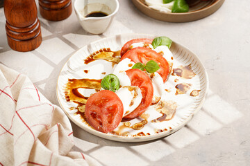 Traditional italian salad caprese consisting of slices red tomatoes, fresh basil and mozzarella cheese with balsamic vinegar dressing on concrete background, wooden pepper and salt mills