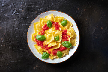 Ravioli with tomato sauce and fresh basil on a plate, shot from the top on a black slate background. Simple healthy Italian dish
