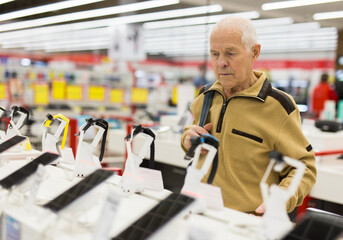elderly grayhaired man pensioner examining counter with electronic gadgets and smart watches in showroom of digital goods store