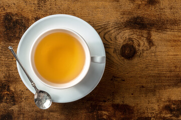 White porcelain teacup, with a saucer and a spoon, overhead flat lay shot on a dark rustic wooden...