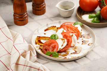 Traditional italian salad caprese consisting of slices red tomatoes, fresh basil and mozzarella cheese with balsamic vinegar dressing on concrete background, wooden pepper and salt mills