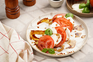 Traditional italian salad caprese consisting of slices red tomatoes, fresh basil and mozzarella cheese with balsamic vinegar dressing on concrete background, wooden pepper and salt mills
