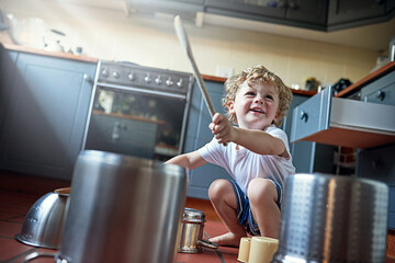 You might call it noise, but kids call it fun. Shot of an adorable little boy playing drums on a set of pots in the kitchen. - obrazy, fototapety, plakaty