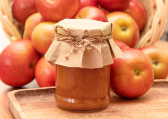 Jar of natural jam with fresh apple packed in kraft paper and tied with a string against the background of a fallen basket of apples on a wooden tray