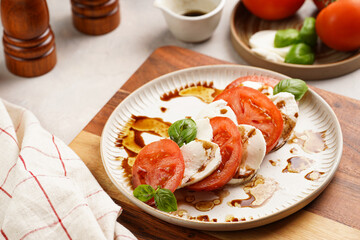 Traditional italian salad caprese consisting of slices red tomatoes, fresh basil and mozzarella cheese with balsamic vinegar dressing on concrete background, wooden pepper and salt mills