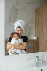 Young mother with baby in towels after shower in bathroom. Concept of hygiene and cleanliness.