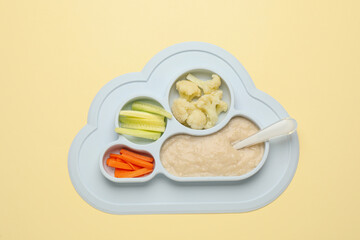 Healthy baby food in plate on yellow background, top view