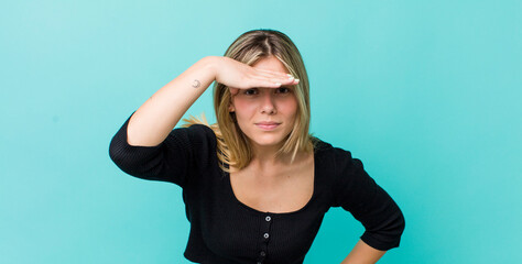 young pretty blonde woman looking bewildered and astonished, with hand over forehead looking far away, watching or searching