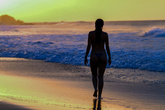 Woman walking alone in Brazilian beach at colorful sunset. Fernando de Noronha island, Brazil