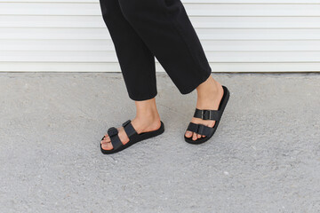 Women's legs in black flat sandals. Trendy female footwear. Summer women's shoes. Details of...