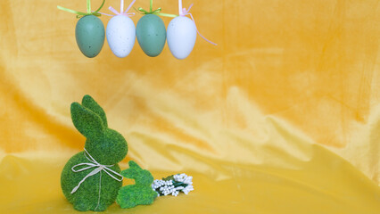 Dekoracje na wielkanoc, zielone zajączki i nakrapiane, wiszące jajka, pisanki na żółtym tle