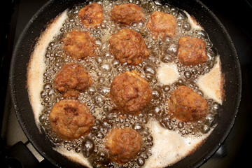 Meatballs frying in a pan, bubbles from the hot oil. Isolated on black background.