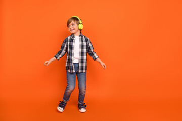 Fototapeta na wymiar Full size photo of young cheerful boy look empty space listen radio melody headphones isolated over orange color background