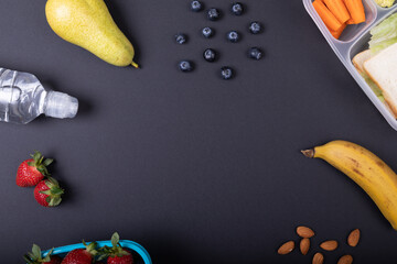 Directly above shot of healthy food and tiffin box by water bottle over black background, copy space