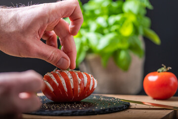 Hand beim anrichten einer Caprese, Tomaten mit Mozzarella und Basilikum, Nahaufnahme