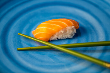 Sushi mit Reis und Lachs samt Stäbchen auf blauem Teller