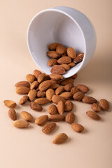 Close-up of almonds spilling from bowl against beige background