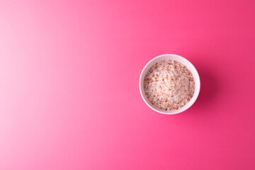 Directly above shot of himalayan rock salt in bowl on pink background with copy space