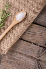 Foto op Plexiglas Close-up of white rock salt in wooden spoon by rosemary on jute fabric at table © wavebreak3