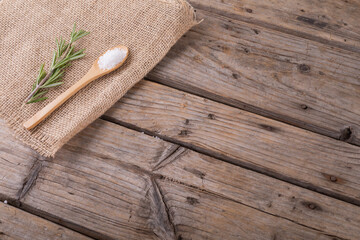 Fototapeta na wymiar High angle view of rock salt in wooden spoon and rosemary on jute fabric at table with blank space