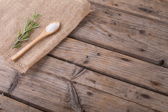 High angle view of rock salt in wooden spoon and rosemary on jute fabric at table with blank space