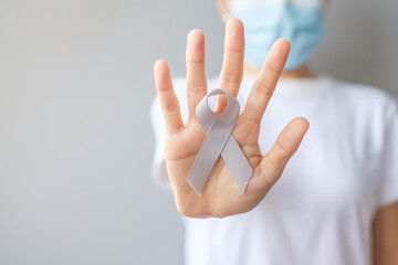 Naklejka premium Brain Cancer Awareness month, woman hand holding grey color Ribbon for supporting people living. Healthcare and World cancer day concept