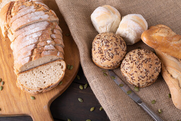 High angle close-up of sliced bread loaf on serving board by buns and baguettes on jute fabric